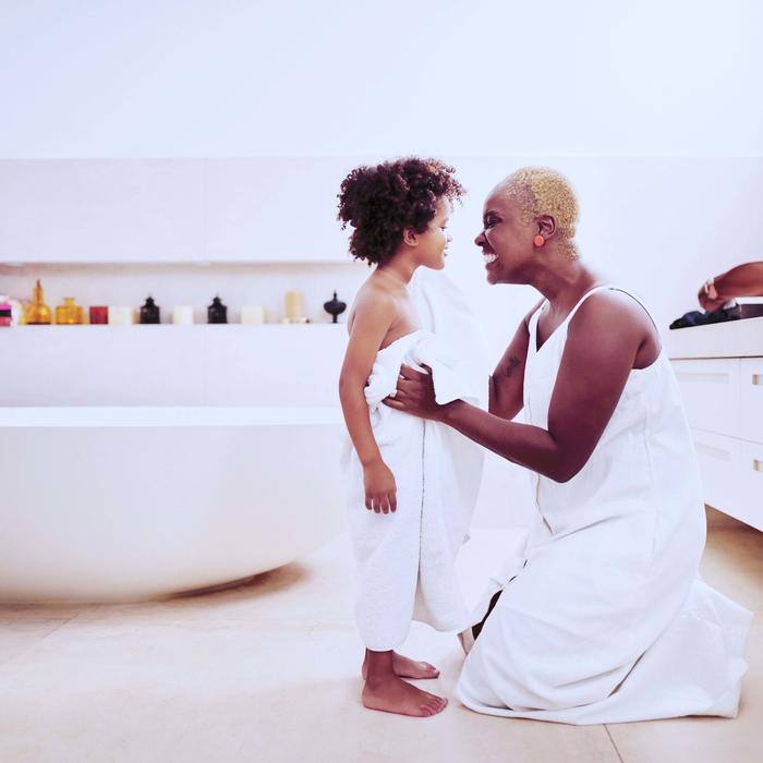 Woman holding daughter while smiling next to bathroom tub