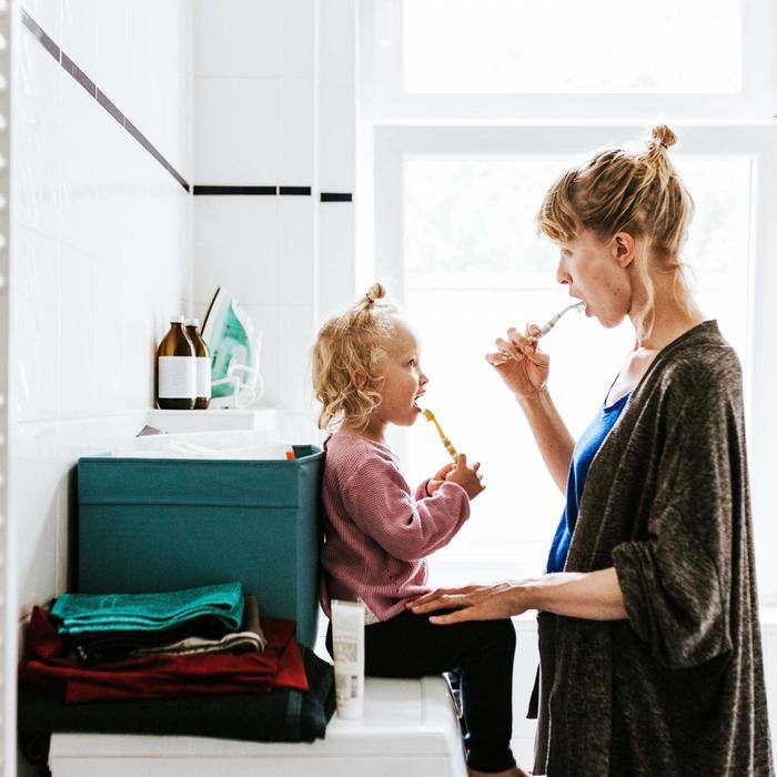 Woman brushing teeth with daughter in brightly lit bathroom