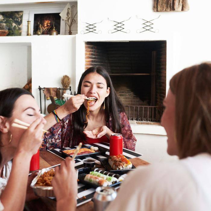 Friends sitting in living room eating sushi with chopsticks