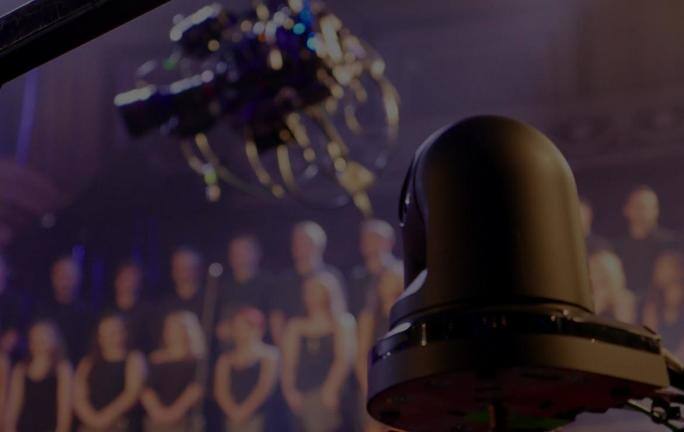 Professional PTZ camera in foreground with blurred audience in background.