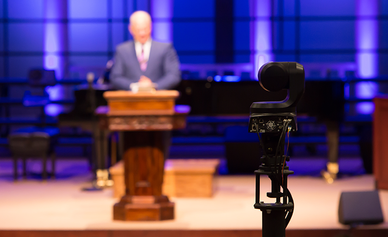 Caméra PTZ professionnelle en concentration avec un homme flou sur le podium en arrière-plan de l'église.
