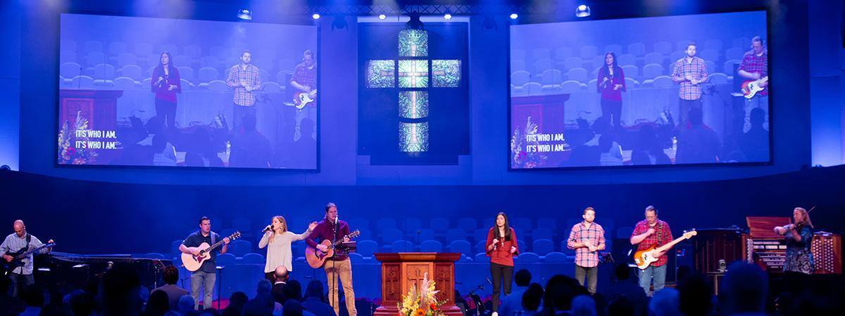 Un groupe se produisant sur scène dans une église avec une grande croix en arrière-plan.