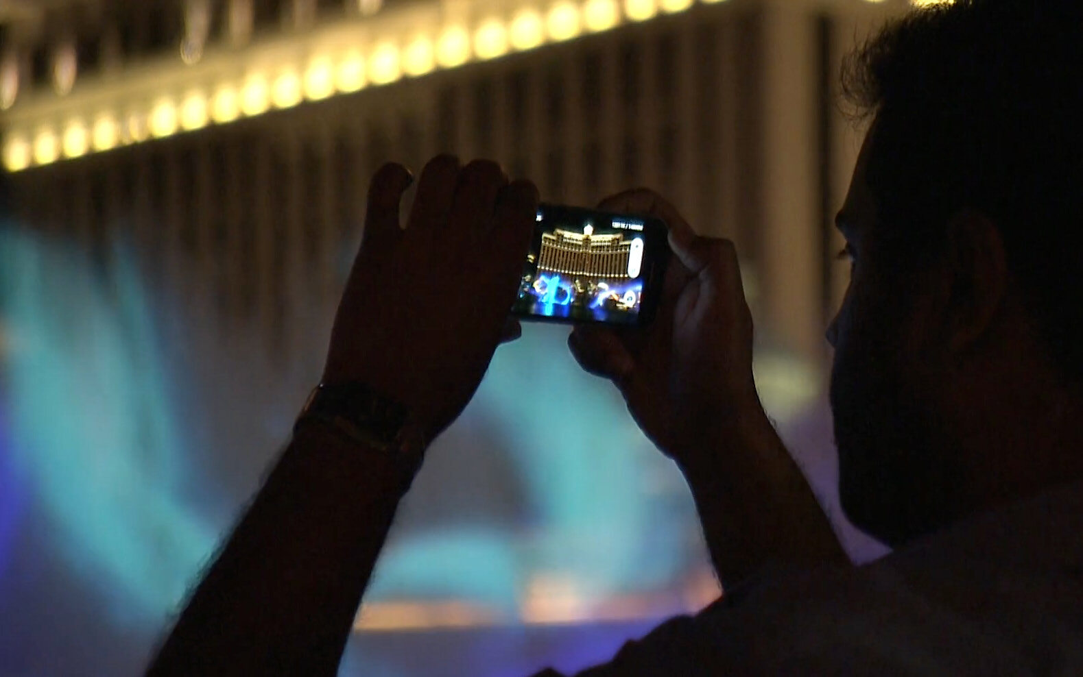 Un homme capturant un bâtiment illuminé sur son téléphone le soir