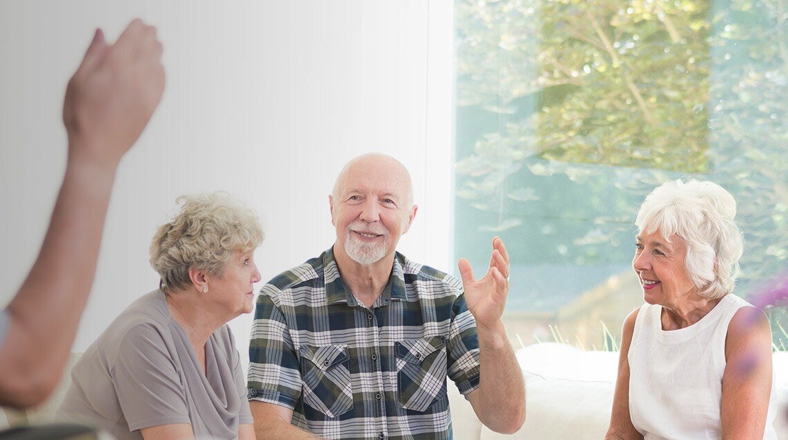 Elderly man waving at friend while talking to two elderly women