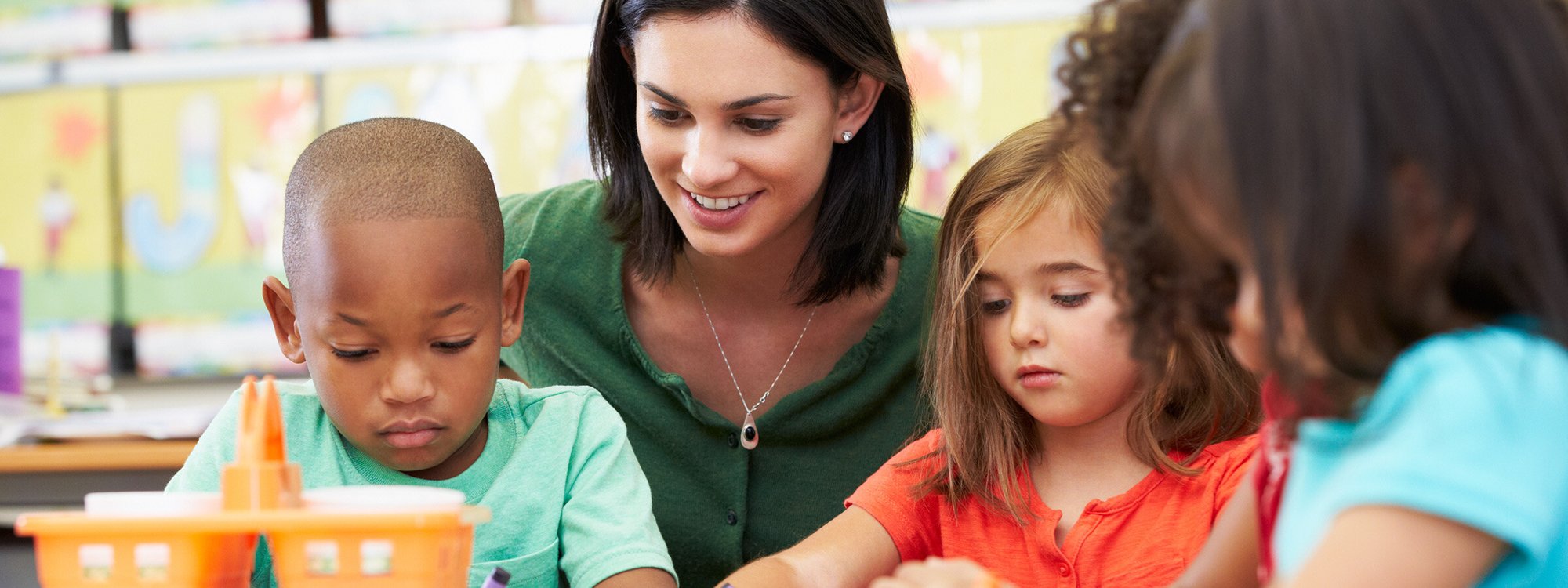 Children in a classroom colour while their teacher watches