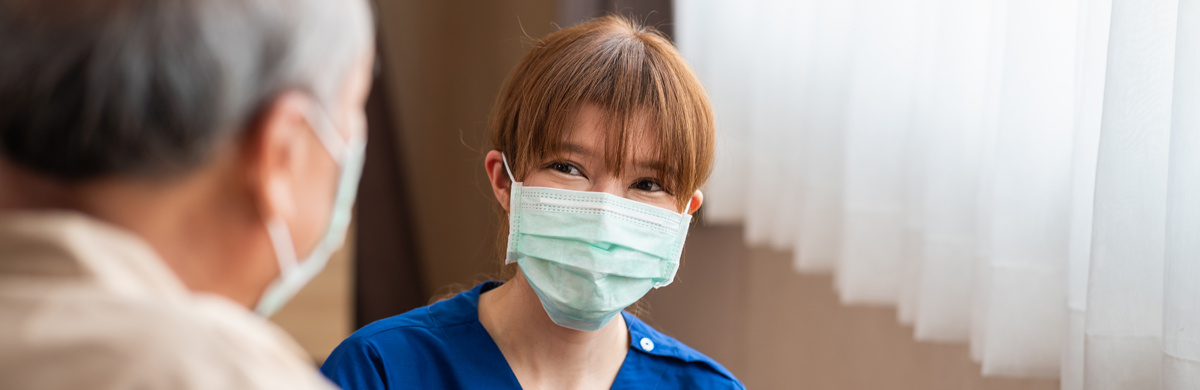 A masked nurse speaks to a senior