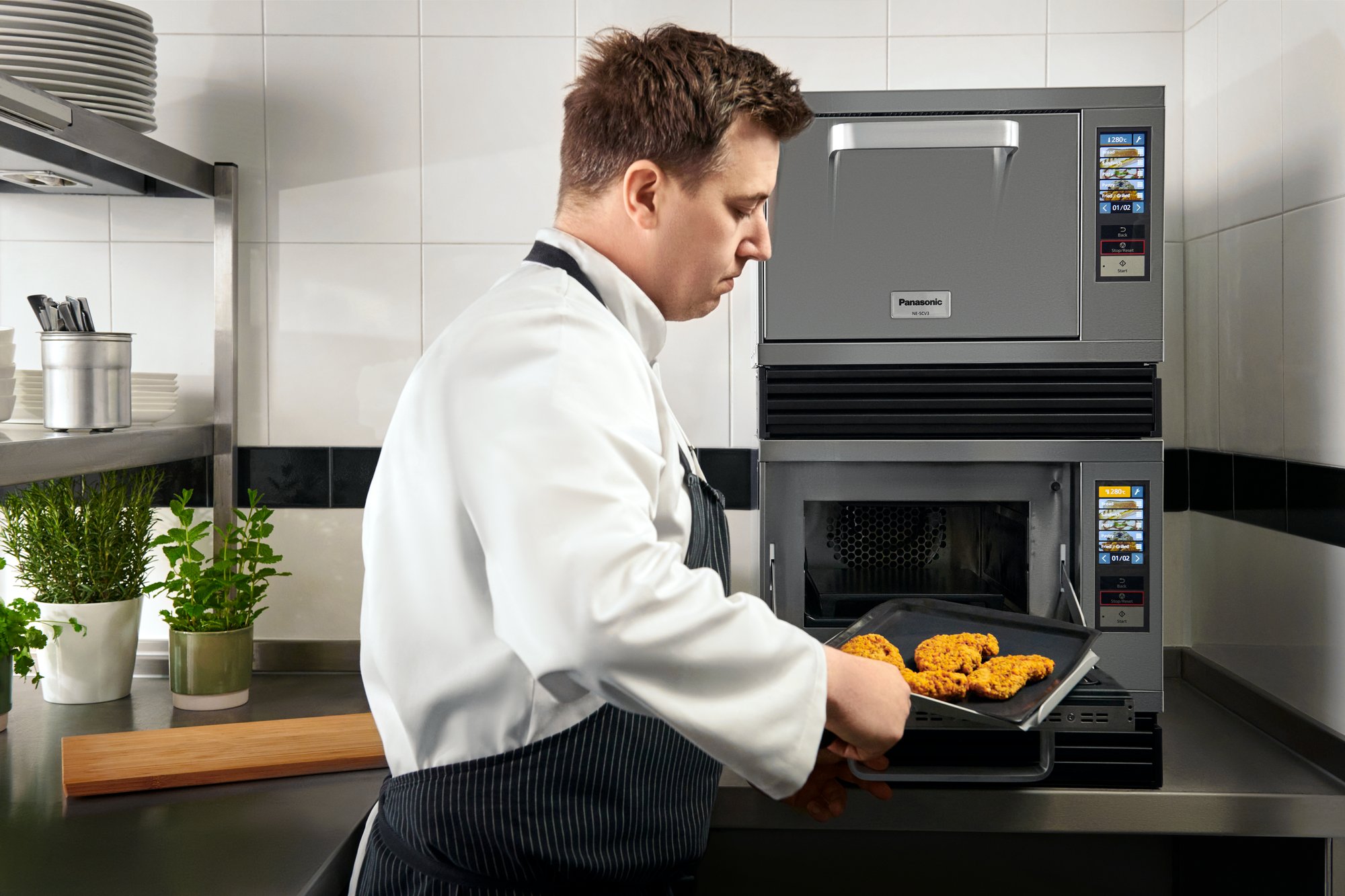 Panasonic NE-SCV3N units stacked on top of one another, with a chef removing cooked food from the bottom oven.