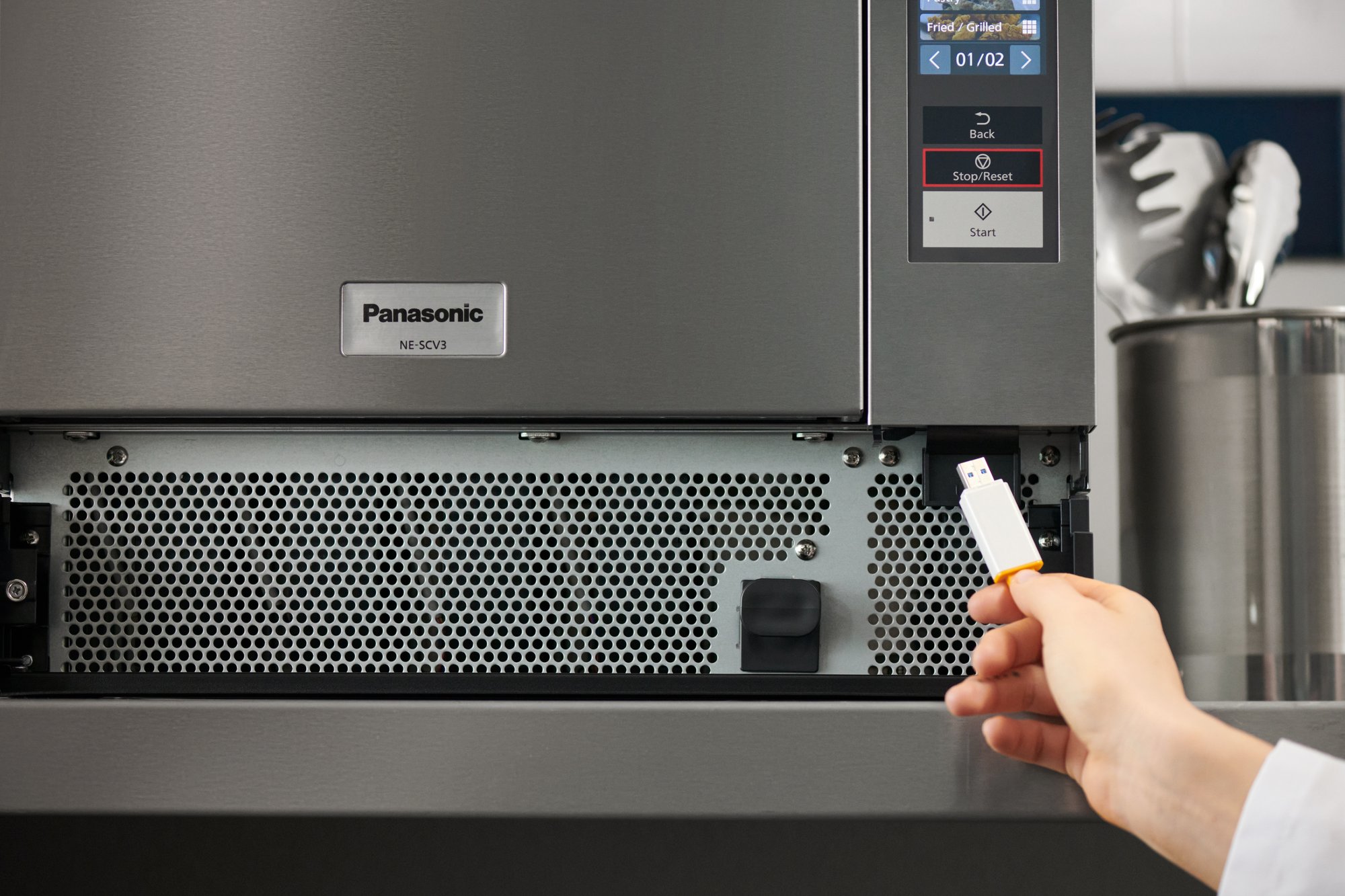 A USB drive is being inserted into a port beneath Panasonic NE-SCV3N as part of the Transfer + menu process shown on the appliance's control panel.