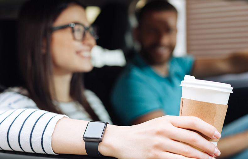 Woman and man sitting in a car, with the woman holding a coffee cup