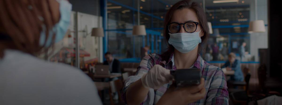 A customer in a mask scans their card on a restaurant payment terminal