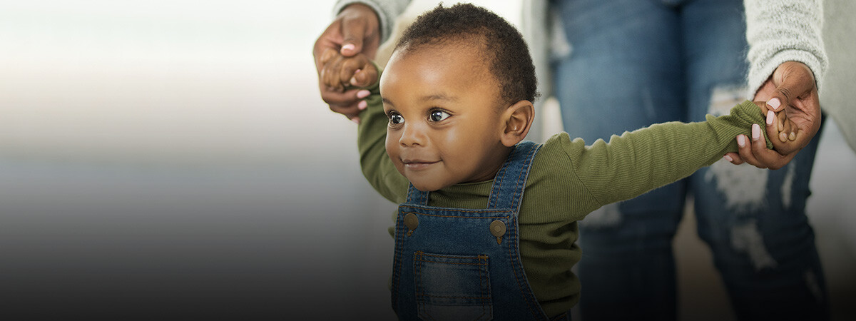 A toddler walks while holding his mother's hands