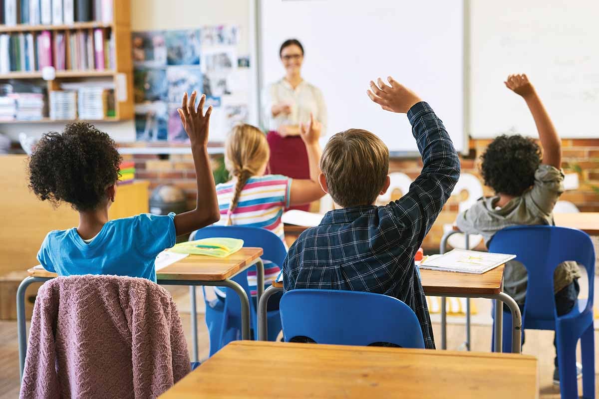 Students sit in a classroom, raising their hands