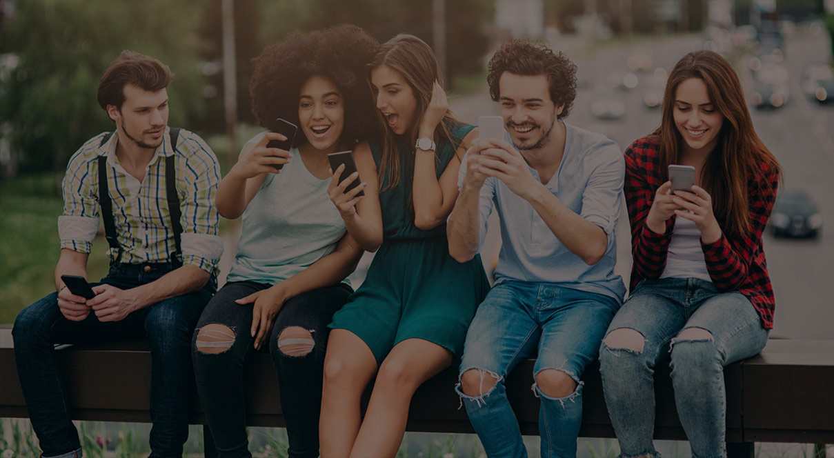 A group of young adults sit outside looking at their phones