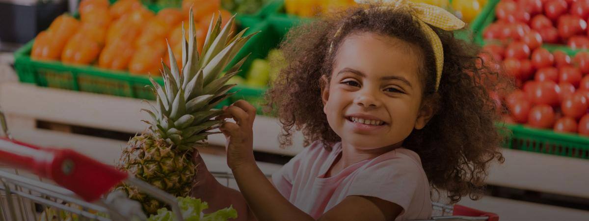 A child in a grocery store holds a pineapple