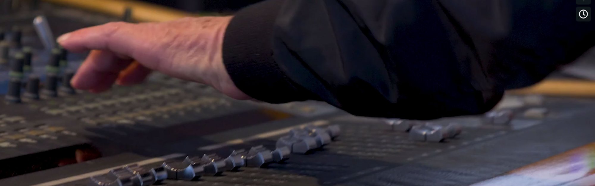 A hand adjusts sliders on an audio mixing board