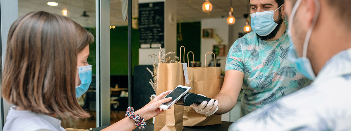 A masked restaurant customer taps their phone to a payment terminal