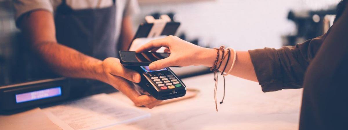 A hand holds a phone to a credit card payment terminal