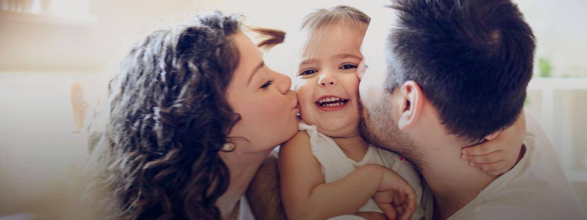 Two parents kiss their baby on each cheek