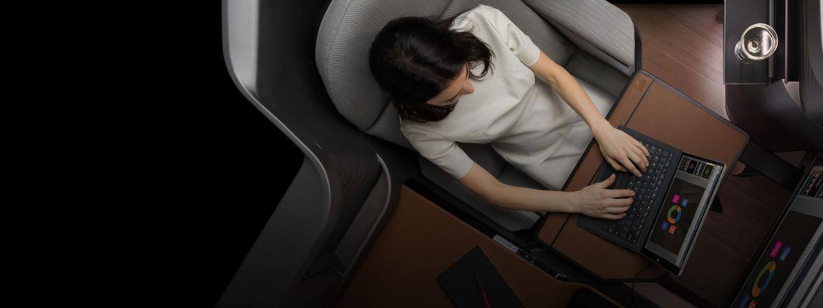 A woman sits in a first class airline seat using a laptop