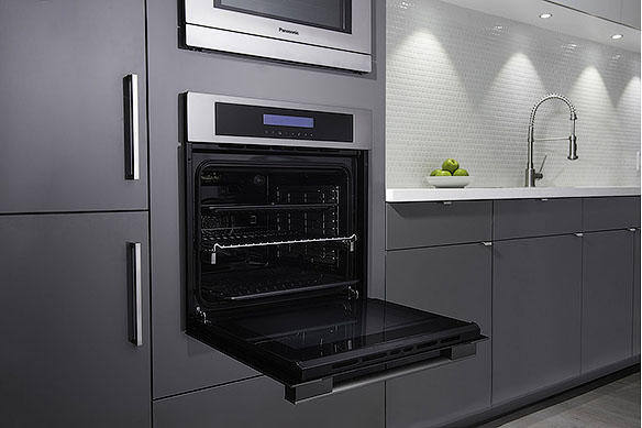 Built-in oven in a modern kitchen with gray cabinets and white backsplash.
