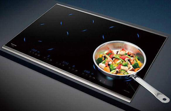Black induction cooktop with a stainless steel pan of vegetables.