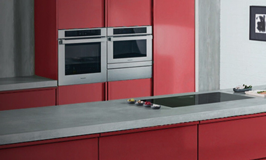 Kitchen with marble countertop and red cabinetry, as well as build-in Panasonic stove, microwave and cooktop