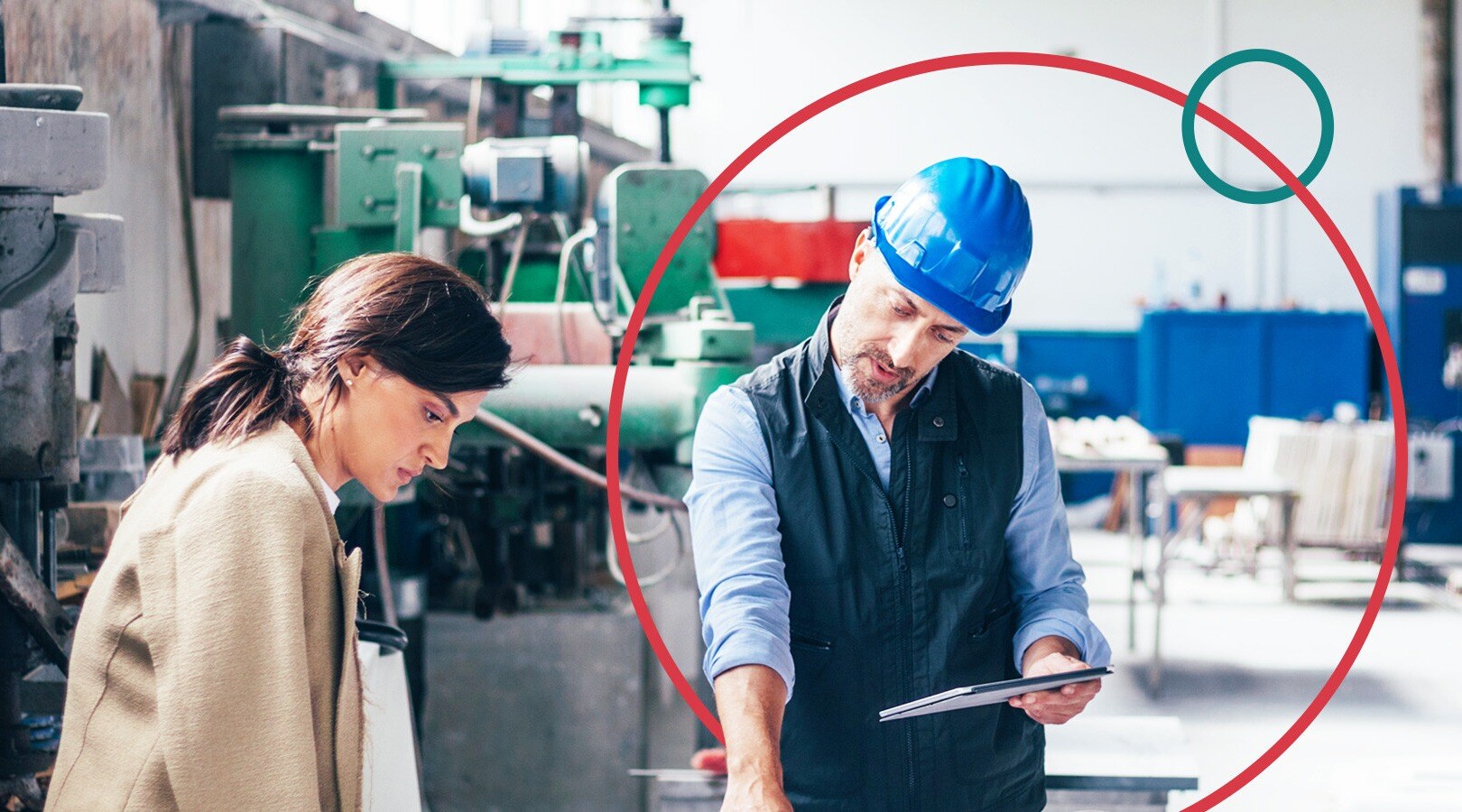 Woman and man staring at blueprints in a factory setting. The man has a blue hard hat on and a tablet in one hand while pointing at the blueprints