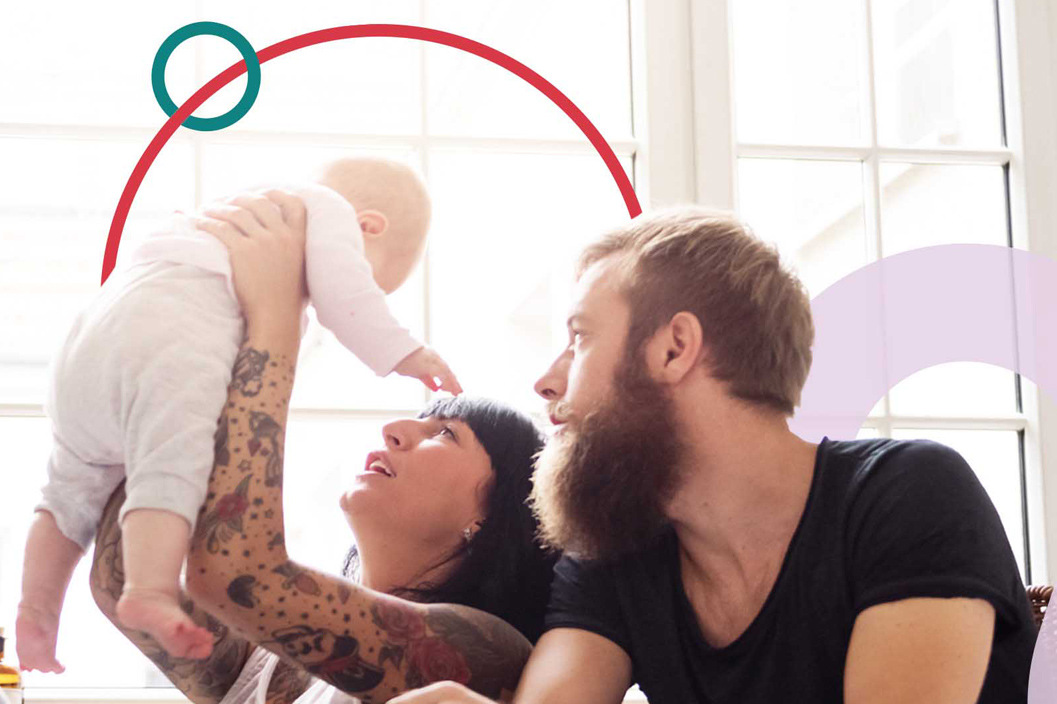 Woman and man holding their baby in the air with sunlight window in background