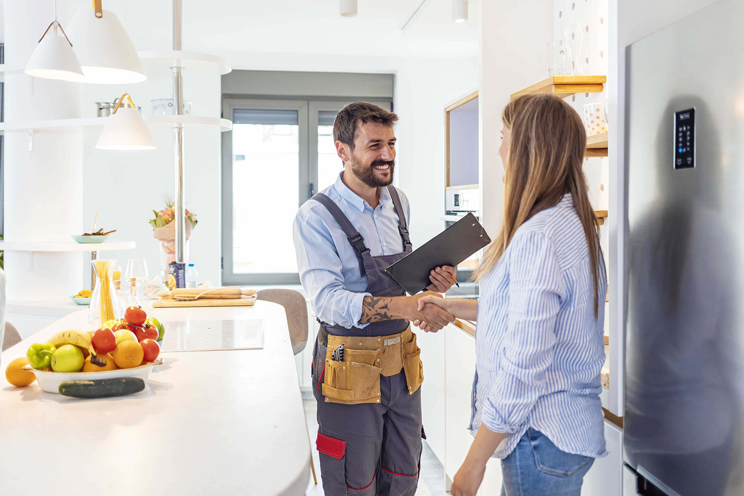 Contractor wearing overalls shaking the hand of woman in a kitchen