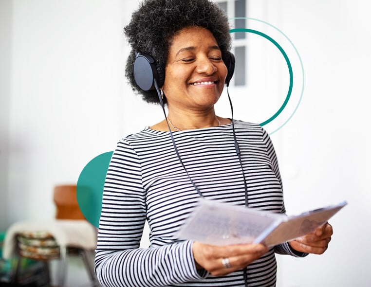 Woman with over the hear headphones on, listening to music and smiling while holding open CD case