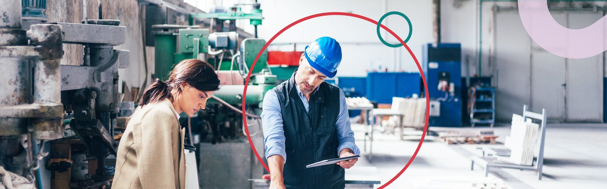 Woman and man staring at blueprints in a factory setting. The man has a blue hard hat on and a tablet in one hand while pointing at the blueprints