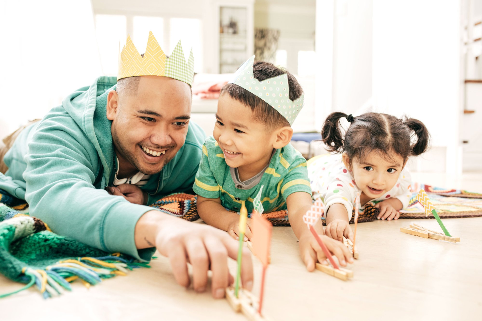 Man wearing paper crown playing with boy wearing paper crown and girl with pigtails