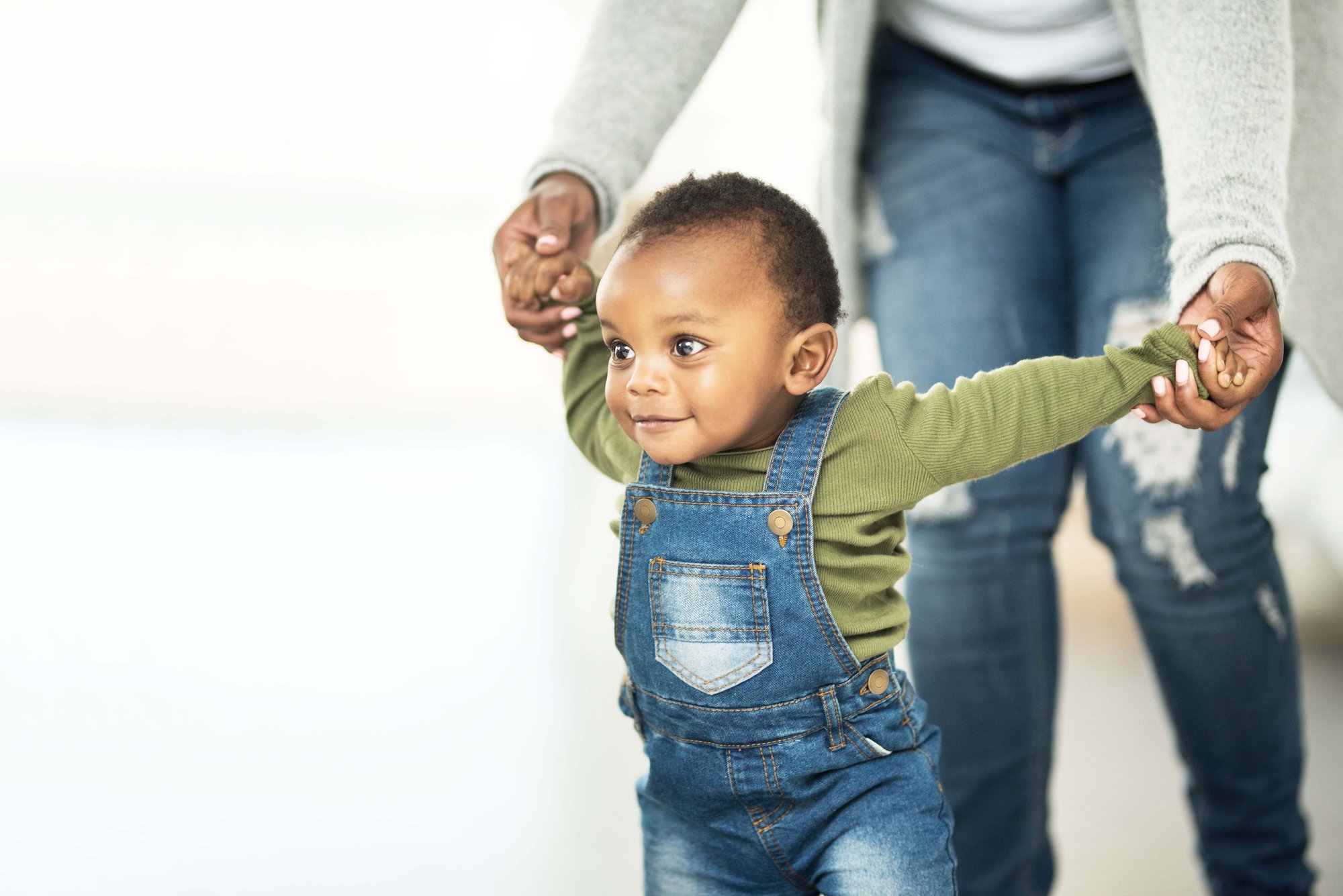 Mother holding baby boy's hands while he walks