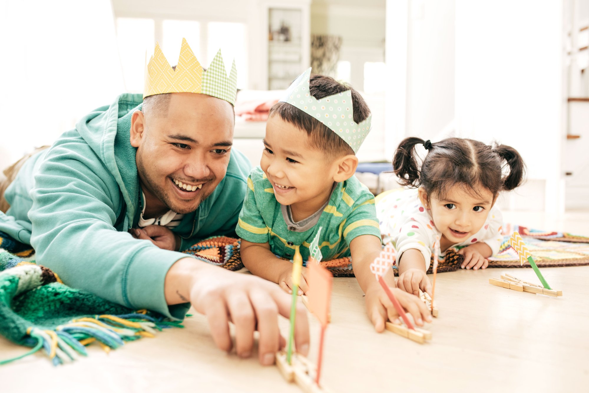 Family playing with colorful paper crowns and toy arrows on the floor.