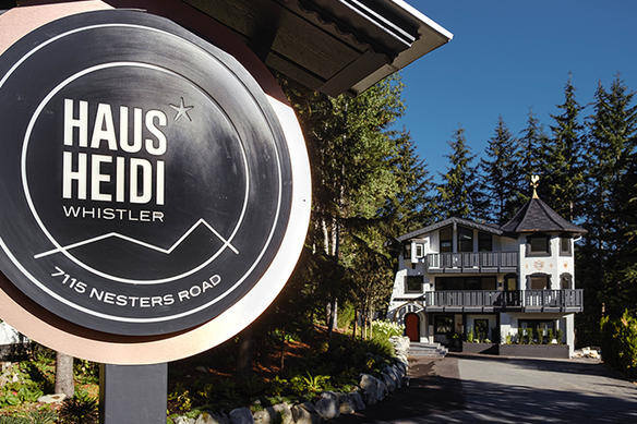 Signe rond lisant "Haus Heidi Whistler" devant une maison à plusieurs étages avec des balcons et des arbres.