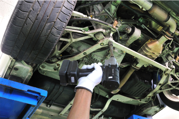 Hand using a tool on a vehicle's undercarriage.