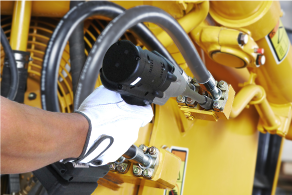 Hand holding a black industrial tool with cables, against a yellow machinery background.