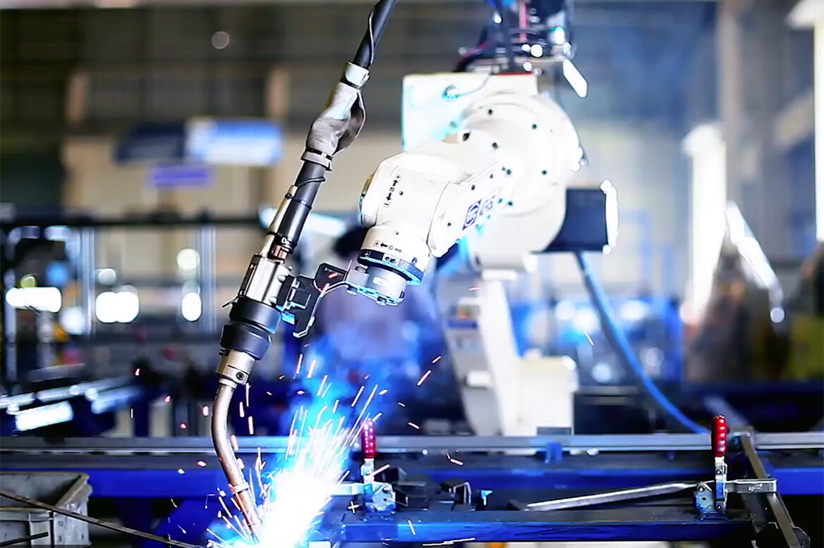 Robotic arm with welding torch attachment welding a component while sparks fly upwards