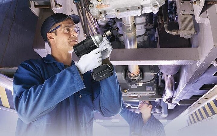 Mechanics holding Panasonic assembly tools working on a vehicle suspended above them