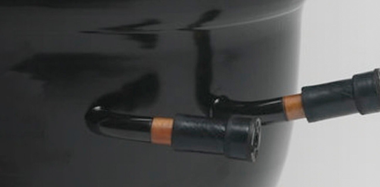 Close-up of a black refrigeration compressor with hose mounts