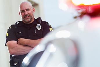 Police officer with arms crossed standing beside police car