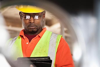 Man wearing yellow hard hat and yellow high visibility vest staring at clipboard