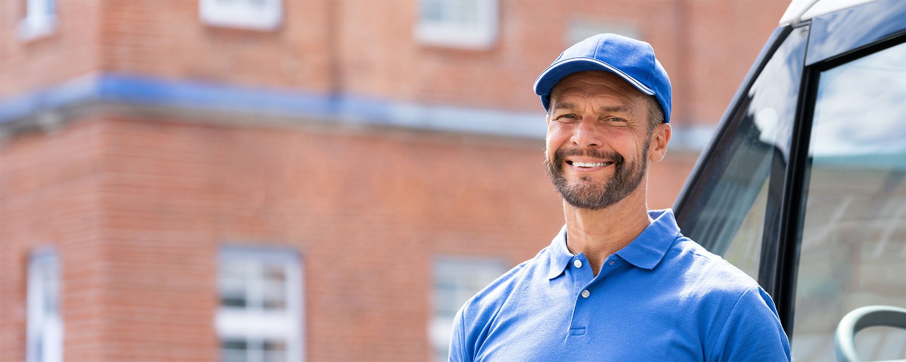Homme souriant en uniforme bleu debout à côté d'une camionnette.