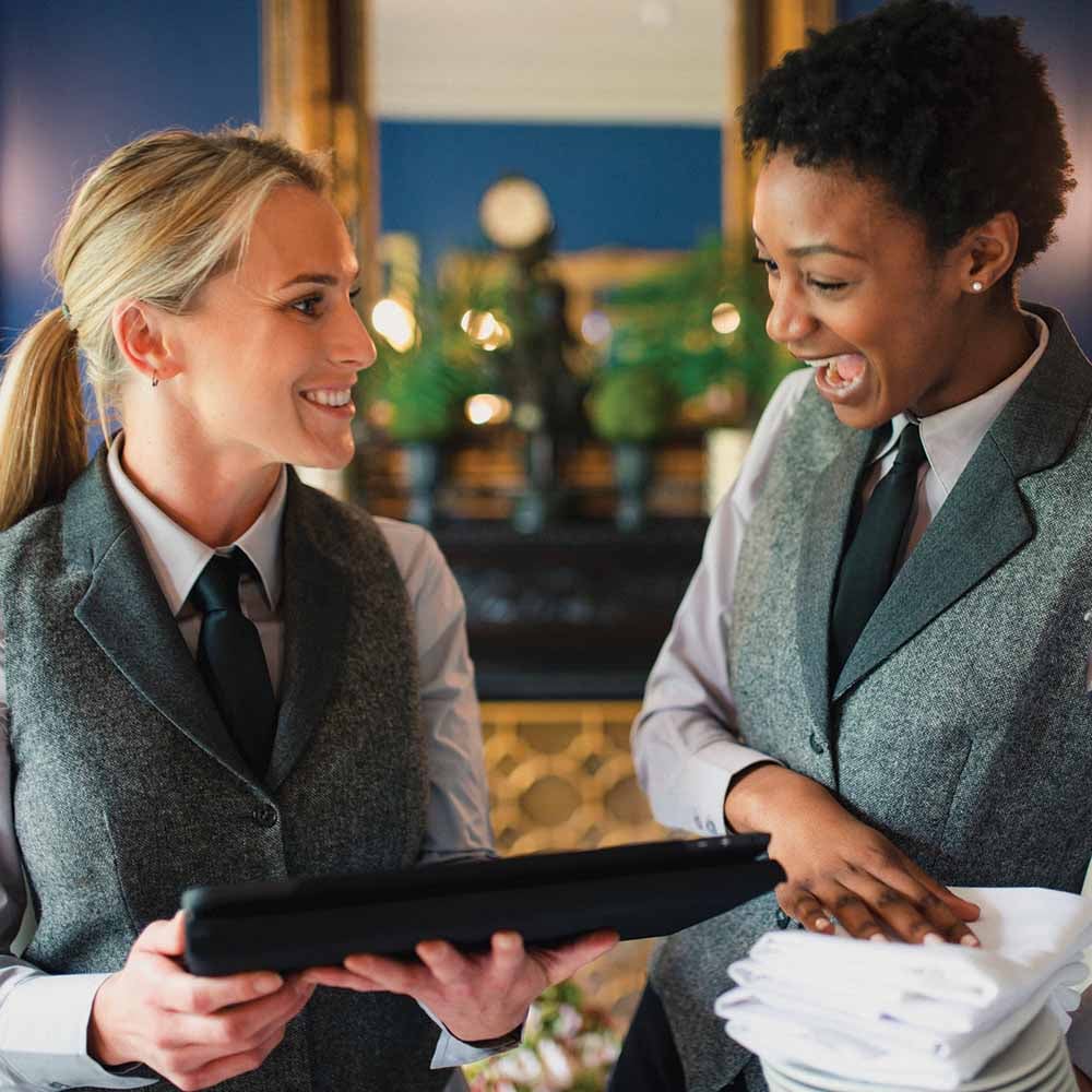 Two hotel staff members smiling and interacting with tablet