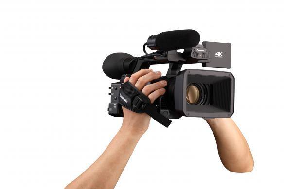 Hands holding a 4K handheld camcorder with a microphone.