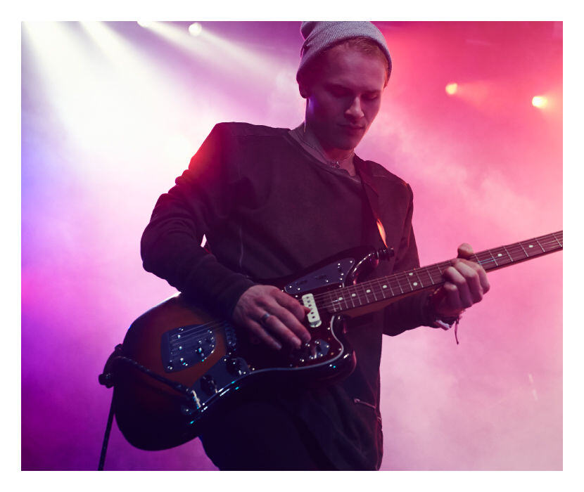 Musicien jouant de la guitare électrique sur scène avec des lumières colorées en arrière-plan.