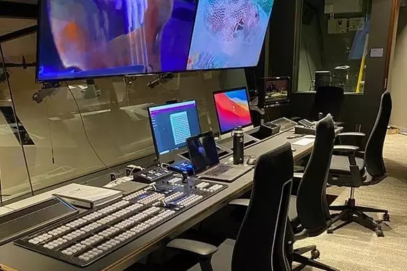 Control room with multiple computer monitors and professional broadcasting equipment.