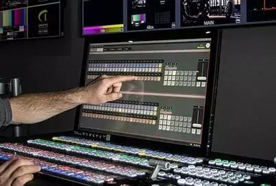 Hand interacting with a live production switcher console in a dark control room.
